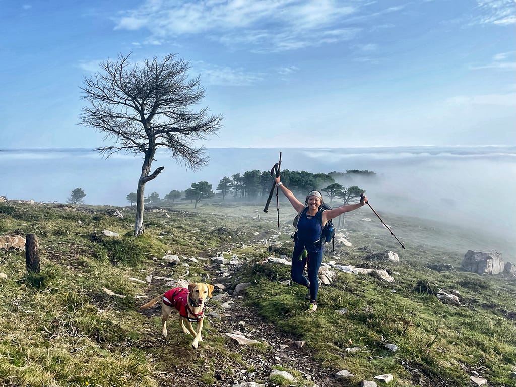 Camino dog and her pilgrim Mom celebrating at the top of the hill above the sea of clouds